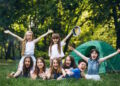 Група щасливих дітей відпочиває на природі біля зеленого намету в літньому таборі в Польщі - Moja Polska